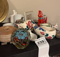 Overview shot of the lot showing flower paperweight, painted pony, piggy bank, wooden bowls with lids, and other ceramic and decorative items.