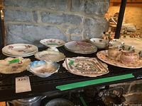 Porcelain trays, cups, saucers, cream and sugar sets arranged on black shelving against stone wall