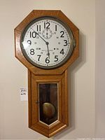 Full frontal view of oak pendulum wall clock hanging on wall