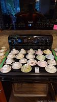 Photo showing the full set of 19 teacups with matching saucers arranged on a stovetop surface.