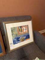 Watercolor painting on couch showing the framed and matted artwork with a gold-tone frame.