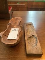 Two wooden items on a wooden table: a carved butter mold with fish designs and a carved burled maple dish.