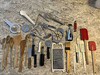 Photo showing assorted wooden spoons, silicone spatulas, metal and plastic kitchen utensils and gadgets arranged on concrete surface.