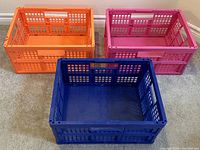 Three collapsible storage boxes in blue, orange, and pink with grid design, positioned side by side.