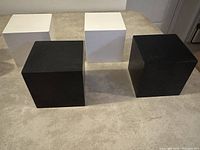Four cube-shaped floating shelves, two black and two white, arranged on carpet floor showing size and colors.