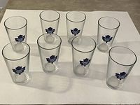 Front view of all 8 pint glasses arranged in 2 rows showing clear glasses with blue Toronto Maple Leafs retro logo.