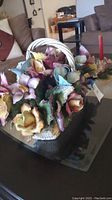 Porcelain flower basket with white handle displaying multicolored flowers on glass top table.
