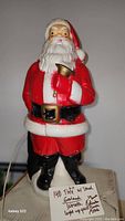 Close-up of plastic Santa Claus figurine holding a bell with a red suit and white beard