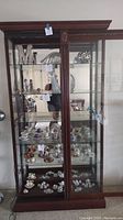 Full frontal view of cherry wood curio cabinet showing glass shelves filled with porcelain and decorative items, not included in sale.