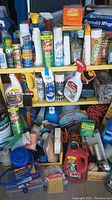 Front view of yellow shelf unit filled with various cleaning products, hardware tools, and household supplies including sprays, cans, foil, polishes, and adhesives.
