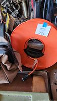 Photo showing orange extension cord wound on large orange reel with black carrying handle and a power plug visible