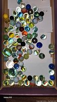 Top-down photo showing a mixed group of vintage glass marbles with colorful swirls and cat eye cores in a box.