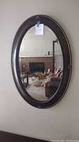 Full frontal view of the oval mirror hanging on the wall reflecting a living room with a fireplace and furniture.