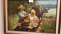 Framed oil painting titled 'Harvest Time' depicting a man and woman on a wooden cart with a water buffalo in a rural landscape.