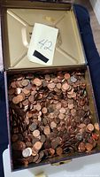 Overhead photo showing open metal collectible tin filled with loose pennies and a paper slip with the number 42 inside the lid.