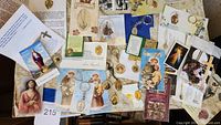 Overview of various prayer cards, religious medals, crosses, and keychains spread on a table, with images of Jesus, Virgin Mary, and saints.
