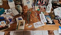 Photo showing a variety of rosaries, crosses, religious books, framed pictures, religious statues, and wood carved hands on a table.