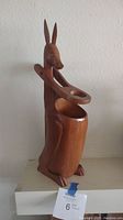 Front view of wooden kangaroo wine bottle holder showing detailed carving and hinged arm.