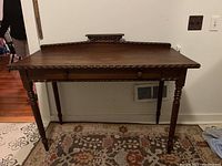 Front view of antique wooden side table showing carved edges, drawer, and turned legs.