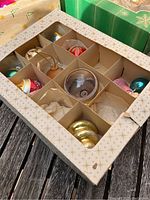 Open box showing 9 compartments with assorted antique and vintage glass Christmas bulbs of various colors and shapes.