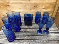 Overview of the entire blue glass set displayed on a wooden table, showing all ten items including glasses and vases.