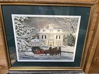 Framed Christmas print showing snowy scene with house and horse-drawn sleigh, captured to illustrate artwork and framing condition.