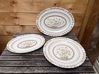 Three serving dishes on wooden surface: two oval platters and one round serving dish with Buttercup floral pattern.