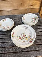 Photo showing stacks of six white Copeland Spode dinner plates with floral patterns, six side plates, and four small bowls on rustic wooden surface.