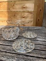 Photo showing all four items on a wooden surface: scalloped edge cake plate on pedestal, round cut crystal dish, flat round flower frog, and cylindrical flower frog.