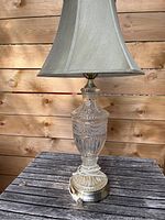 Full view of a table lamp with a fabric shade and detailed glass base set against a wooden background.