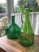 Pair of vintage green bottles on wooden table by window with short squat bottle and tall handled bottle