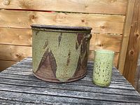 Large green pottery vessel and small green candle holder on outdoor wooden table