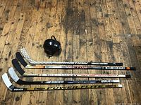Five vintage wooden hockey sticks laid on wooden floor showing brand and model details.