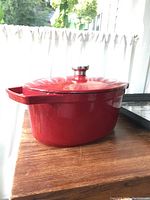 Side view of the red KitchenAid oval casserole dish with lid on, showing integrated handle and stainless steel knob on lid.