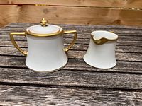 Covered sugar bowl and open creamer side-by-side on outdoor wooden surface.