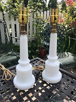 Pair of white milk glass table lamps with hobnail texture on a metal outdoor table, showing full body and brass fittings, no shades.