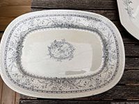 Rectangular floral ceramic platter with central floral medallion and floral border in gray on white ceramic.