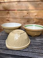 Three beige ceramic Gripstand bowls on wooden surface, one upside down showing embossed exterior.