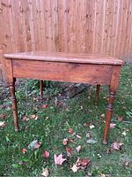 Front view of the small wooden antique table placed outdoors showing rectangular top and turned legs.