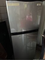 Full view of silver Magic Chef refrigerator indicating small apartment size with top freezer and refrigerator below.