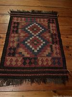 Full view of a small vintage rectangular throw rug showing geometric diamond medallion design in earth tones with fringed edges.