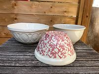 Three ceramic bowls shown on a wooden surface: two white bowls and one with red marbling on white base. One of the white bowls has embossed oval patterns on the exterior.