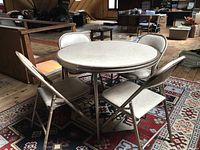 Vintage card table with four matching folding chairs set on patterned rug in room with wood flooring.