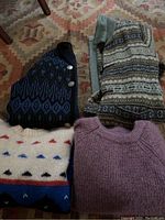 Four vintage sweaters laid out showing colors and patterns including purple knit, cream with multicolor pattern, blue and black button-up, and a Fair Isle pattern sweater.