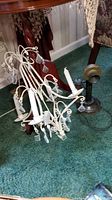 White enameled metal candle chandelier with faceted pendant accents lying on the floor with faux candles visible, photo taken to display chandelier condition and design.