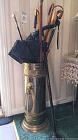 Full view of brass umbrella stand filled with umbrellas, walking sticks, and canes.