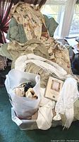 View of various curtains, drapes, sheers, and table runners arranged on a chair with plastic bin beneath