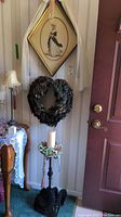 Full view showing wreath, framed Victorian lady print, black metal pedestal candle holder, and feather fan near entry door.