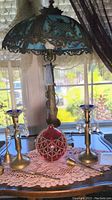 Photo showing stained glass lamp with bronze look metal base, two brass candlesticks with crystals, ruby glass oil lamp with bead netting.