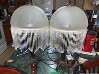 Two matching vintage-style table lamps with frosted glass shades featuring floral etching and beaded fringe trim, placed on a table.